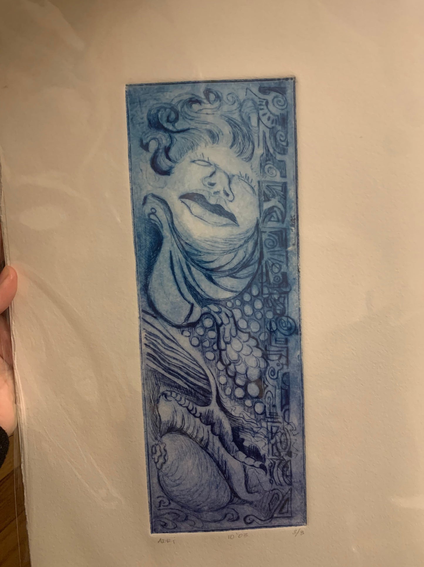 drypoint illustration in blue and indigo vertically oriented featuring an abstract face and organic elements like a bird tail, leaf, conch shell and geometric shapes